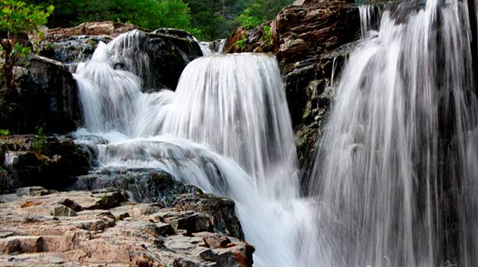 A cascading waterfall flowing over rocky terrain with lush green trees in the background.