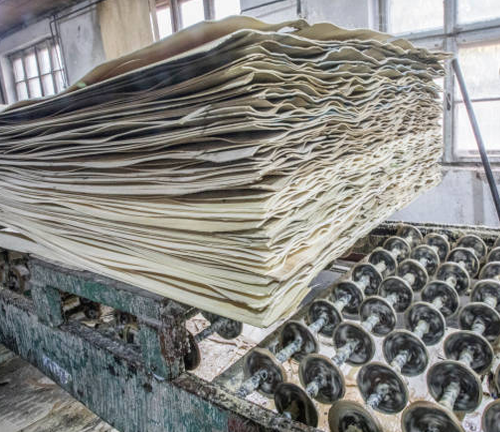 A large stack of processed paper sheets rests on a machine in an industrial setting, showcasing the production process in the pulp and paper industry.