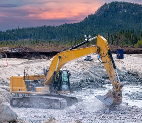 A yellow excavator digging into rocky terrain at a mining site with a forested mountain in the background, under a colorful sunset sky, representing industrial extraction activities in natural environments.