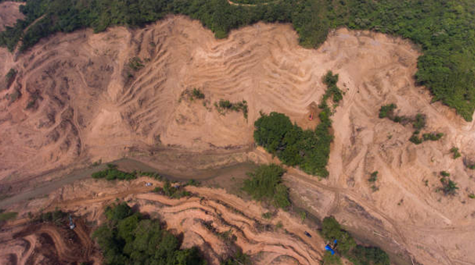 Aerial view of a deforested rainforest area showing extensive land clearing, soil degradation, and remaining patches of green forest, highlighting the environmental impact of deforestation.