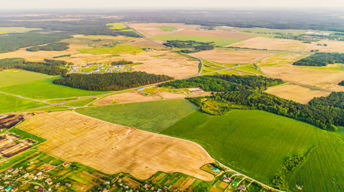 Aerial view of a patchwork of agricultural fields and small forested areas, with rural settlements and roads interspersed throughout the landscape.