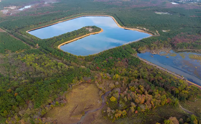 Aerial view of a man-made lake with strategically designed peninsulas surrounded by diverse forest terrain, illustrating advanced land and water management for biodiversity conservation.