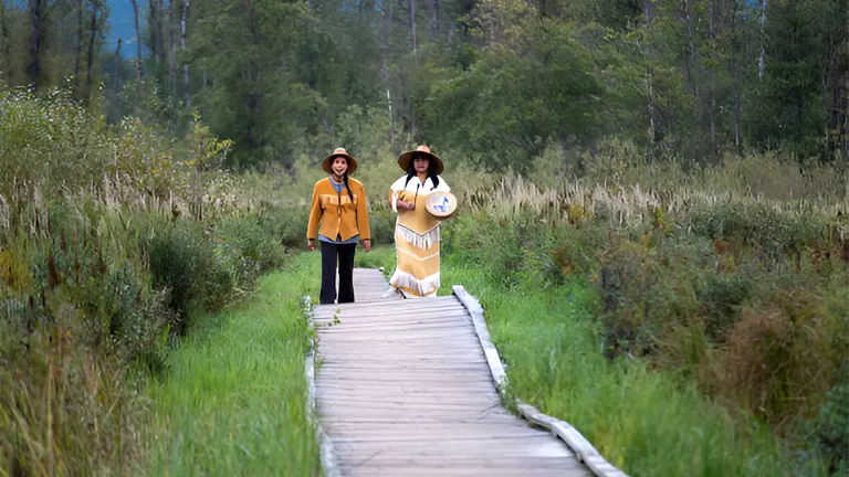 Two women walking on a boardwalk through a forested area, illustrating community involvement in sustainable forest management.