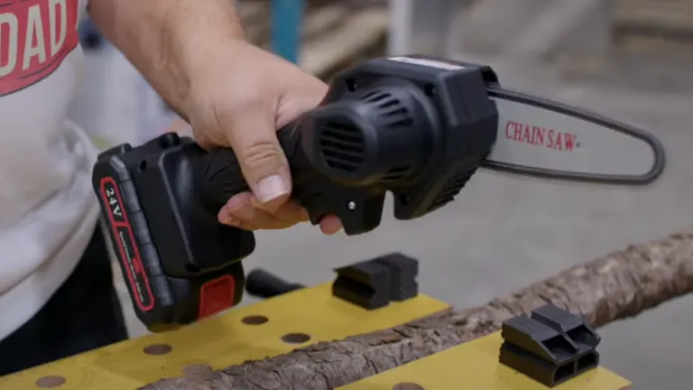 Person holding a 24V Woodwise Mini Chainsaw near a branch for review demonstration.