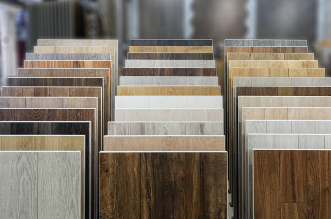 A display of various wood-patterned laminate flooring samples in different shades, ranging from light to dark brown. The organized arrangement highlights a variety of textures and finishes for customers.