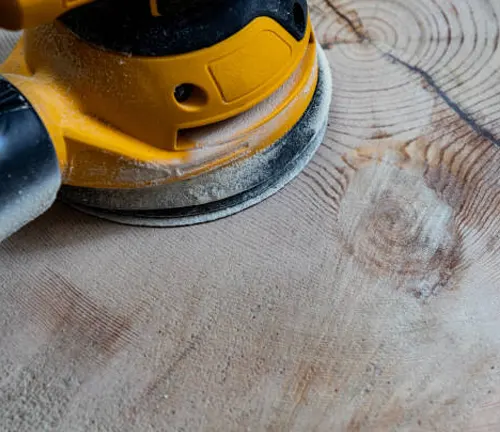 Electric sander on timber surface showing dark machine burn marks from overheating.