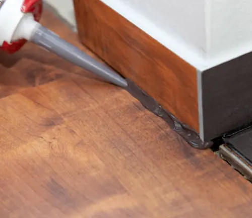 Applying gap filler with a caulking gun to seal gaps between floor and baseboard.