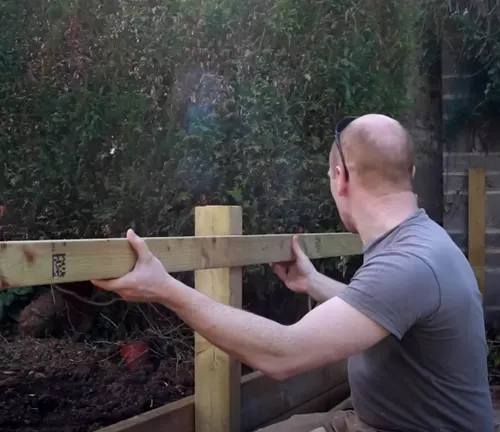 Man installing wooden horizontal rails for a privacy fence in the backyard.