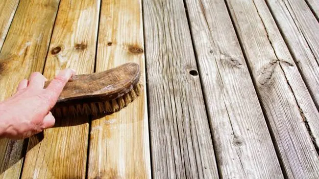 Hand scrubbing timber floorboards, showing a transition from weathered to clean wood surface.