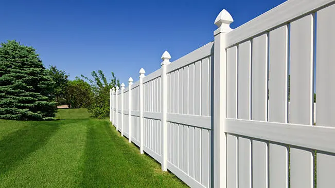 A long white vinyl fence with posts standing in a well-maintained grassy yard.