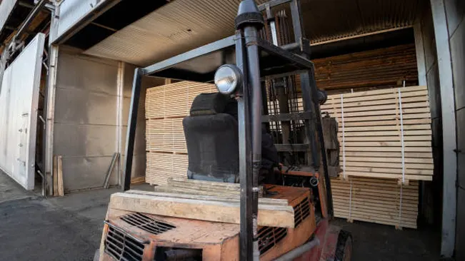 Forklift transporting lumber into a kiln, showcasing technology used to monitor moisture content accurately.