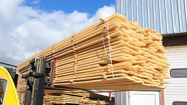 Forklift moving a large stack of graded softwood lumber outside a warehouse facility.