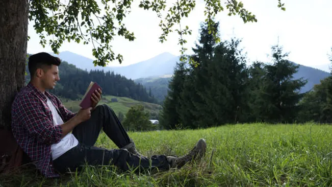 Man reading under a tree in nature, emphasizing continuous learning and staying informed.