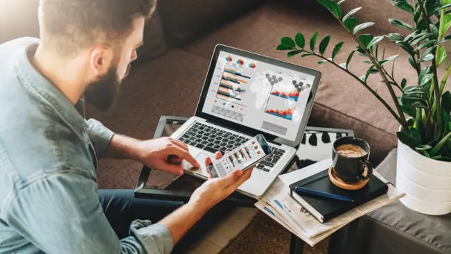 Man analyzing data on laptop and smartphone for timber marketing trends strategy.