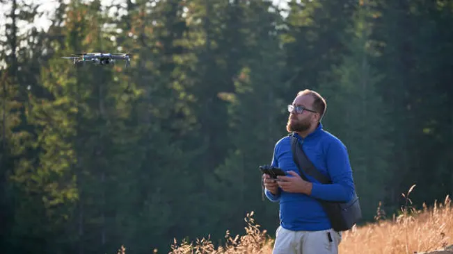 Person using drone for forest monitoring, highlighting technological advancements in modern forestry management.