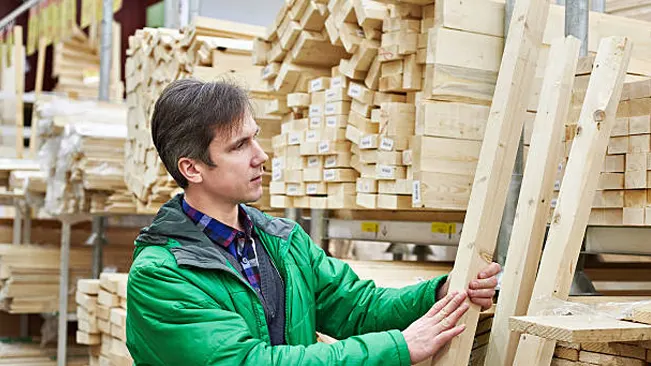 Man inspecting lumber in a store, focusing on wood quality and selection.