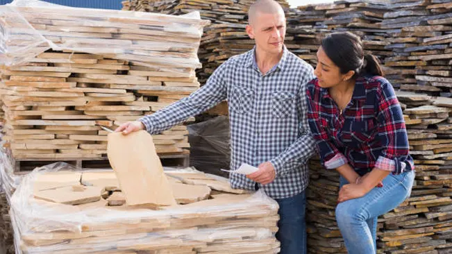 A man and woman discussing and inspecting custom-milled timber products for sale in bulk.