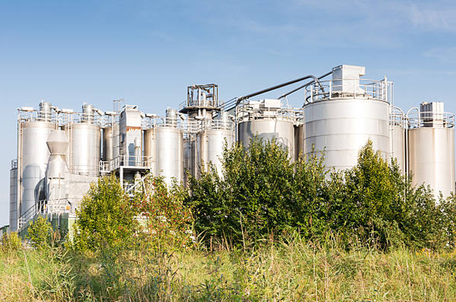 "Industrial biofuel plant with large metal storage tanks surrounded by greenery, representing sustainable energy production and the integration of industrial facilities with nature."