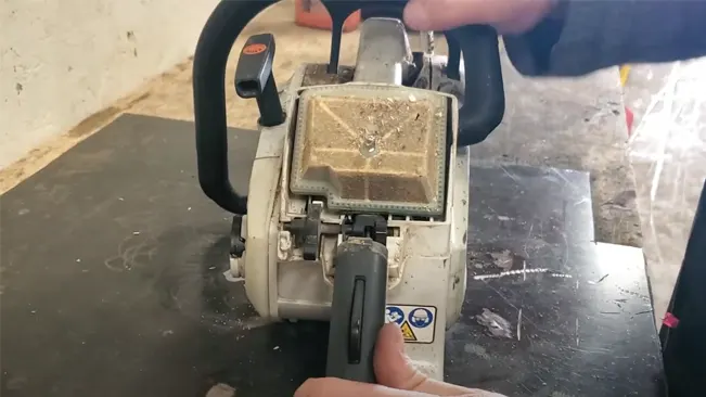 Using a vacuum to clean a dusty chainsaw air filter on a flat surface