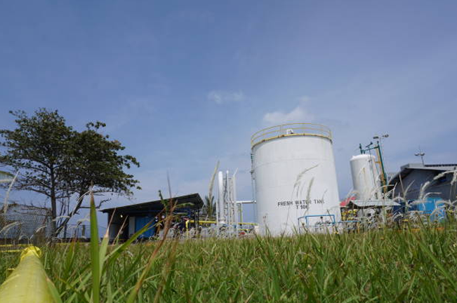 Large white storage tank labeled 'Fresh Water Tank' in an industrial setting, surrounded by green grass and trees, symbolizing a blend of industrial and natural environments.