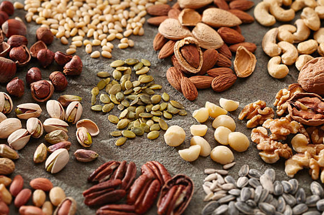 A variety of nuts and seeds displayed on a textured surface, including almonds, walnuts, cashews, hazelnuts, sunflower seeds, and pumpkin seeds, showcasing diverse forest harvests.