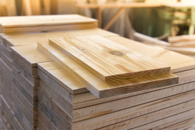 A stack of neatly cut wooden boards is displayed in a workshop. The top board showcases a smooth surface with natural wood grain patterns, highlighting its quality for construction or carpentry.