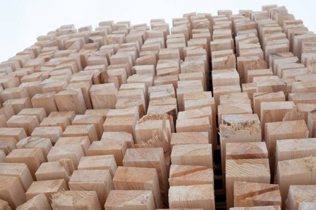 Close-up view of stacked wooden beams, evenly cut and arranged in a dense pattern, showcasing the precision and preparation of lumber for construction or industrial use.