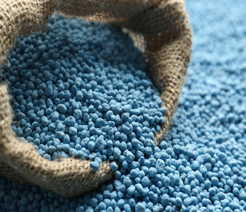 A burlap sack spills out small blue granular fertilizer, commonly used in agriculture and forestry to provide essential nutrients like nitrogen, phosphorus, and potassium.