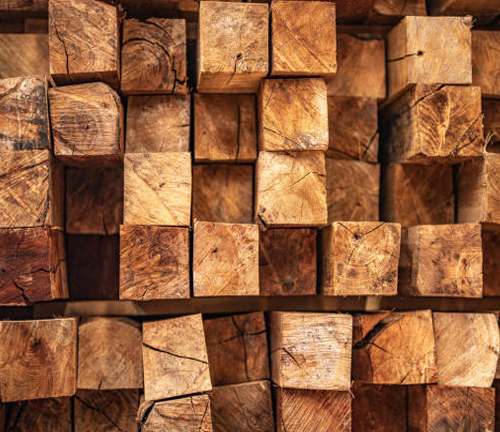 A close-up view of stacked, square-cut lumber pieces, showing the natural grain and texture of the wood, prepared for construction or woodworking projects.