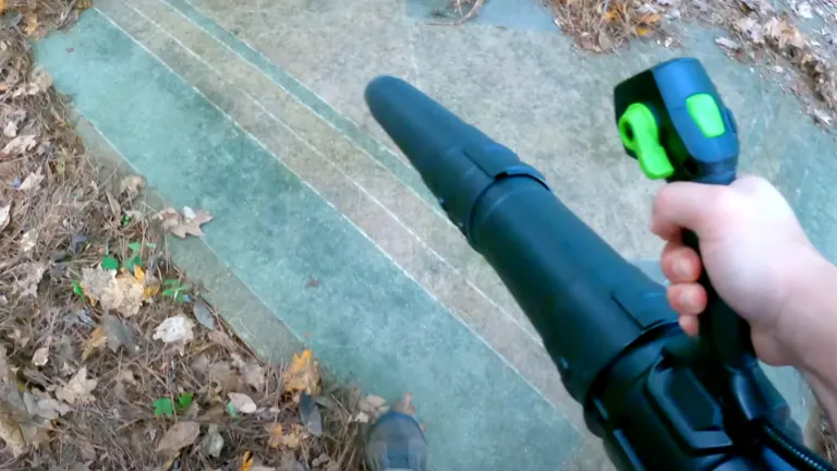 User operating the Greenworks Pro 80V leaf blower to clear leaves from a concrete surface.