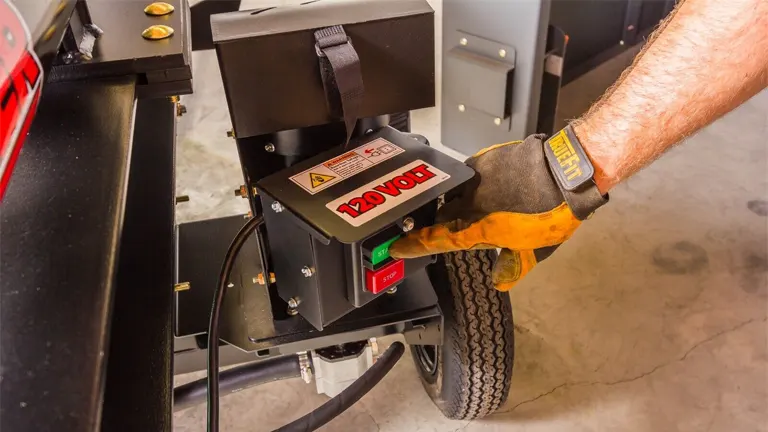 Close-up of hand pressing the start button on a 120V Swisher LS22E log splitter.