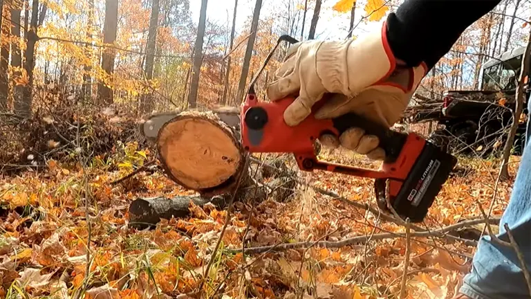 Person using a Milwaukee M18 FUEL mini chainsaw to cut a log outdoors in a forest during fall.