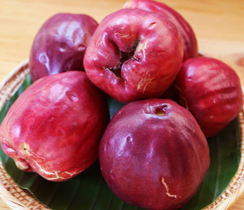 Several ripe, red rose apples arranged in a basket.