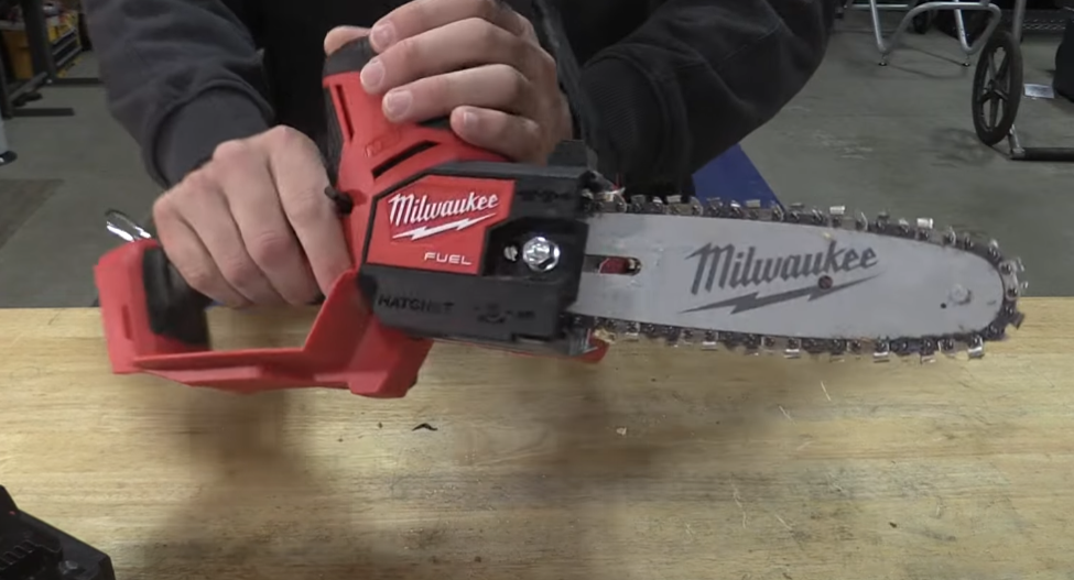 Person holding a Milwaukee M18 FUEL Hatchet mini chainsaw, showcasing its design and features on a workbench.